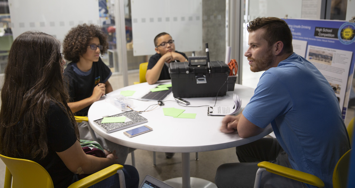 three high school students sitting talking to college student