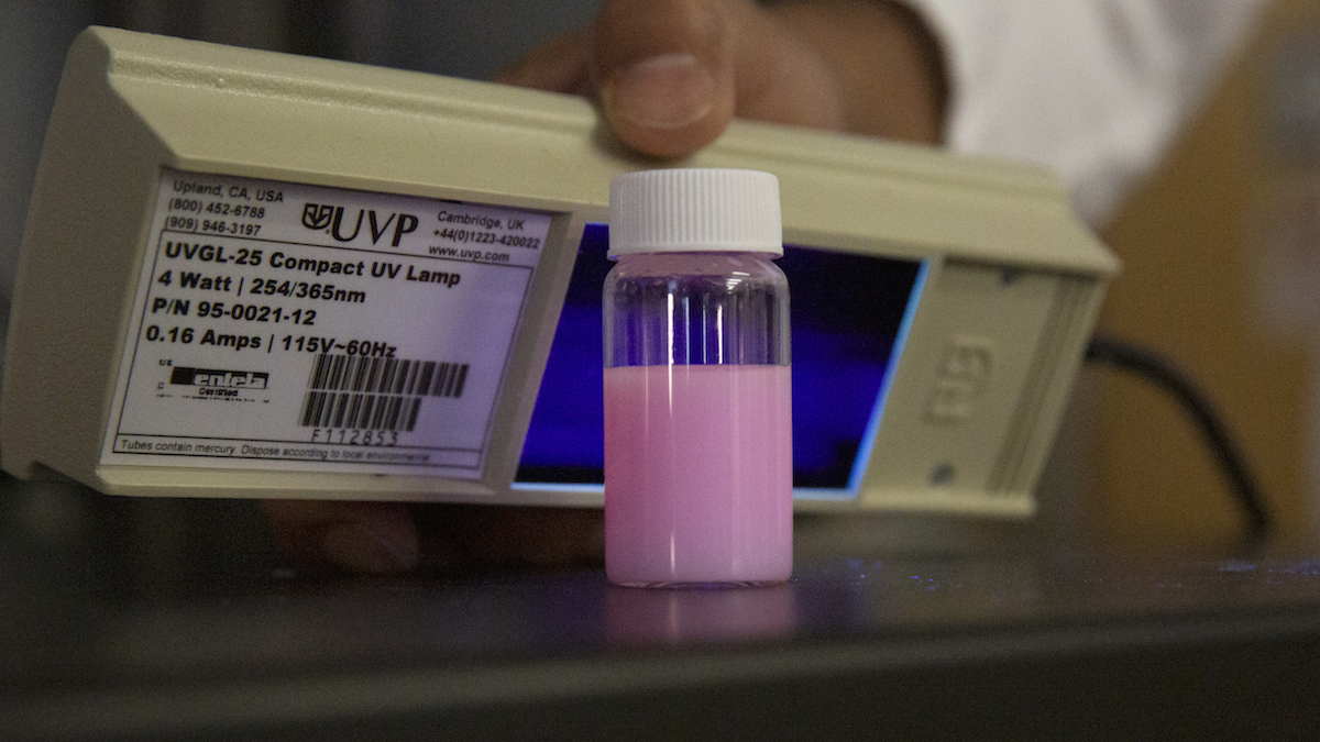 container of pink liquid in front of a UV lamp